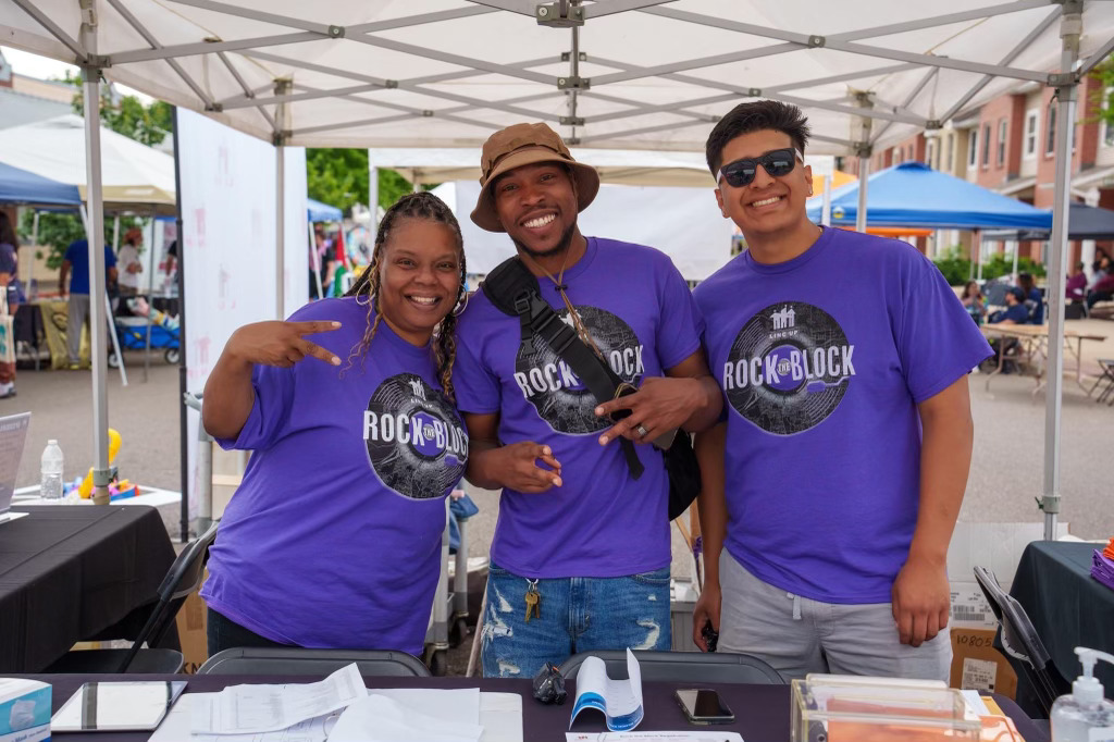Individuals smiling under a tent wearing purple t-shirts with screen printed design